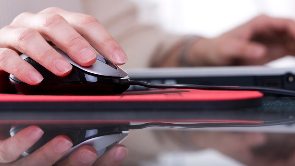 Une main tient une souris d’ordinateur, devant un ordinateur portable
