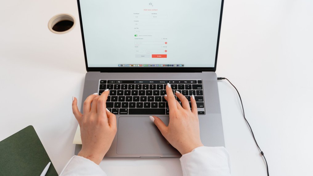 Les mains d’une personne sur le clavier d’un ordinateur portable qui affiche un formulaire en ligne