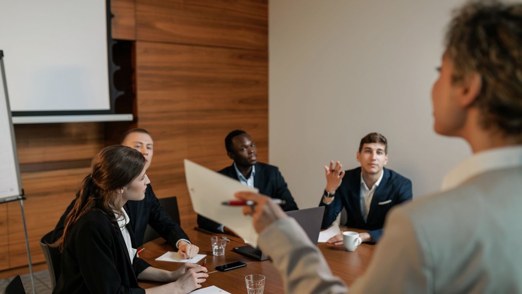 Réunion autour d’une table dans une salle lambrissée : plusieurs participants échangent, l’un tend un document