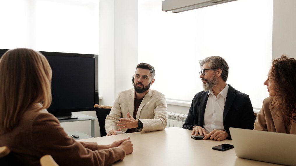 Quatre salariés en discussion autour d’une table de réunion, dans une salle claire ; un homme parle en faisant un geste de la main, les autres l’écoutent.