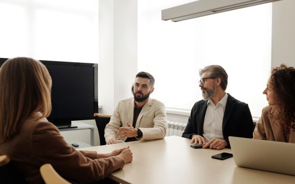 Quatre salariés en discussion autour d’une table de réunion, dans une salle claire ; un homme parle en faisant un geste de la main, les autres l’écoutent.